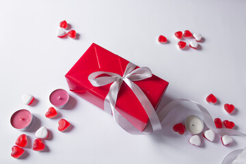 Present box in red paper with silver ribbon bow. White background with jelly hearts and candles. Holidays sale concept.