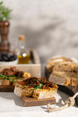 Ciabatta bread sandwich with humus and dried tomatoes, arugula leaves on white table. Italian traditional food - bruschetta, antipasto. with ingredients. Copy space. 