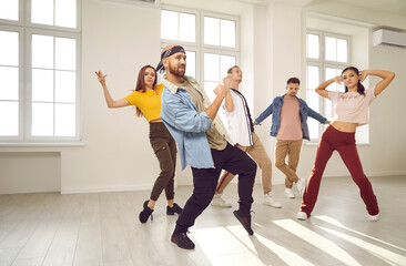 Group of happy young dancers in a modern dance studio. Different cheerful, beautiful, talented people in trendy casual wear enjoying a dancing class, moving to the music and having fun together