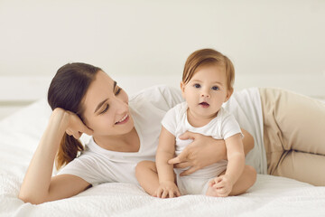 Mothers day.Portrait of cute baby infant on bed at home with smiling young Caucasian mother. Happy mom play relax maternity leave with newborn kid. Planned motherhood and fertility.Childhood concept.