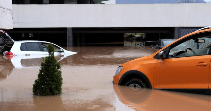 Torrential rain causes flash floods in the city area. Cars under water in the condominium parking lot.  Residential buildings surrounded by water. Damaged cars caused by heavy rainfall. 
