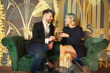 Loving middle aged couple on couch with drinks on coffee table in hotel lobby