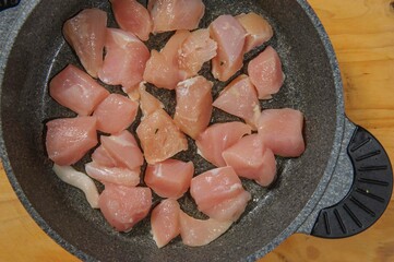 Raw chicken cubes in bowl on dark bowl. Breast cubes. Top view. Copy space.