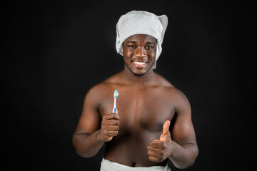 portrait of a happy African male in a towel on his head with a toothbrush with a hand gesture 