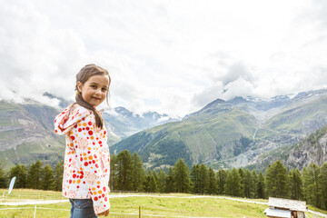 Children hiking in Alps mountains. Kids look at snow covered mountain. Spring family vacation. Little girl on hike trail in alpine meadow. Outdoor fun and healthy activity.