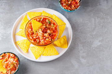 Salsa dip and nacho chips on a white plate. Tortilla chips and salsa sauce in bowl on a gray background. Mexican cuisine. Top view. Copy space