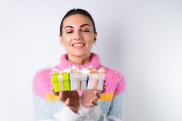 Young cheerful girl in a soft colored sweater on a white background holds small cute gift boxes