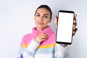Obraz premium Young cheerful girl in a bright colored sweater on a white background holds a big phone in focus with a blank white screen