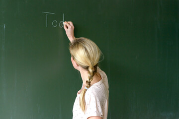 Female teacher writing with chalk on a chalkboard