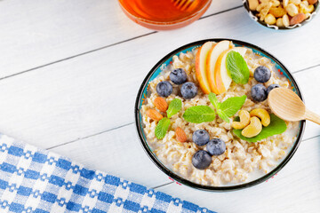 Oatmeal bowl and honey on a white boards. Oatmeal porridge with blueberries, apple slices and fresh mint. Healthy breakfast. Top view. Copy space