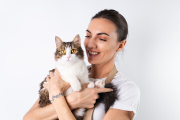 A young housewife in an apron on a white background holds her beloved pet, a big fluffy cat, a happy family