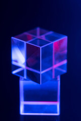Optical glass cube on neon color blurred background. Colored backdrop with geometric shapes, soft selective focus.