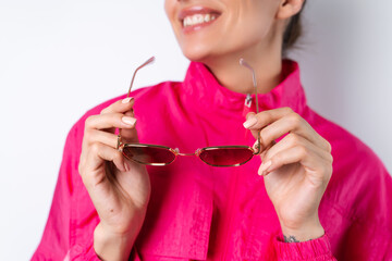 Stylish young woman in a bright pink sports jacket, holding trendy sunglasses in focus on a white background