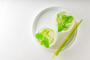 Mojito cocktail and glass straws on white background. Two glasses of mojito on a white tray. Summer vacation concept. Copy space
