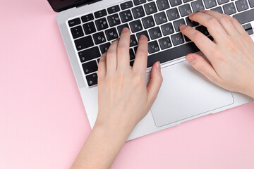 Female hands and laptop keyboard on a pink background. Concept workspace, work at the computer, freelance and design. Flat lay, top view and copy space photo