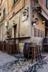 Finalborgo, Finale Ligure, Italy. May 5, 2021. View of a typical trattoria wine bar restaurant in Via del Reclusorio with wooden barrel-shaped tables outside.