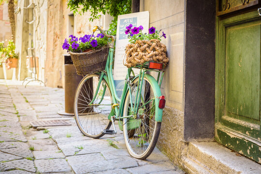 Finalborgo, Finale Ligure, Italy. May 5, 2021. In a small street in the center an old green bicycle leaning against a wall with wicker baskets with flower pots inside.