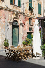 Fototapeta na wymiar Finalborgo, Finale Ligure, Italy. May 5, 2021. In a small street, wooden tables outside a restaurant in Piazza del Tribunale.