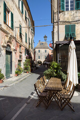 Fototapeta na wymiar Finalborgo, Finale Ligure, Italy. May 5, 2021. In a small street, wooden tables outside a restaurant in Piazza del Tribunale. In the distance, Piazza Aicardi.