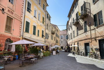 Fototapeta na wymiar Finalborgo, Finale Ligure, Italy. May 5, 2021. View of Piazza Aicardi with outdoor tables of bars and restaurants.