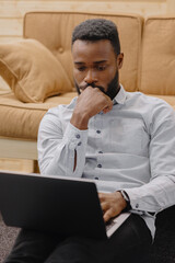 a handsome and young African American man in an office or coworking works on a laptop, talks on the phone or takes notes in a notebook. african american male businessman marketer or financier, modern