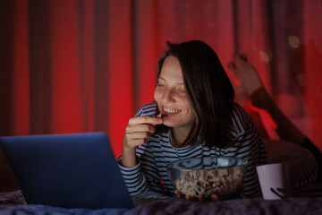 a woman in a striped sweatshirt and hat eats popcorn and watches a movie on TV or a TV series at...