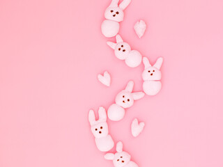 Pink handmade marshmallow candy bunnies in wave shape on pink paper background with copy space for your Easter text message. Minimal happy Easter holiday conceprt. Top view flat lay, border frame.