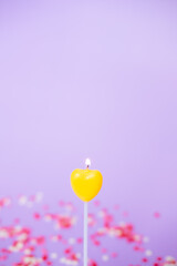 yellow candle in the form of a heart close-up on a purple background. Valentine's day and birthday concept