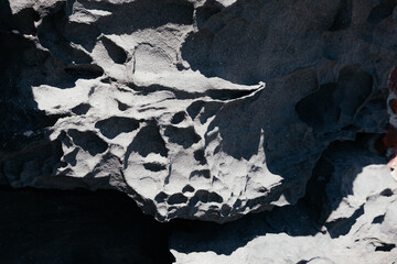 Cracked rough dark grey rock stone texture surface background. Part of mountain outside. Seamless natural backdrop with shadows and sun light. Dark stone grunge background. Mountain texture. Closeup.