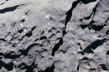 Cracked rough dark grey rock stone texture surface background. Part of mountain outside. Seamless natural backdrop with shadows and sun light. Dark stone grunge background. Mountain texture. Closeup.