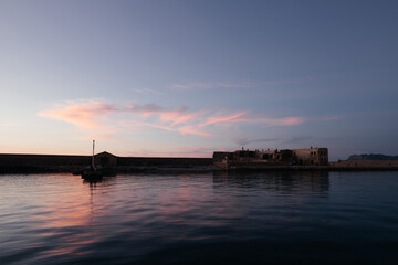 Venetian harbour near lighthouse in old harbour of Chania with nice sunset reflection on water of sea; Crete; Greece. Long exposure. People watching sunset from the harbour. Nice background.