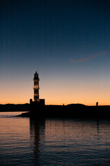 View of old venetian harbour waterfront and lighthouse in sunset time in old harbour of Chania, Crete, Greece. People silhouettes watching sunset at Chania Lighthouse on Crete, Greece. Copy Space