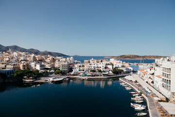 Fototapeta na wymiar Beautiful view of small town Agios Nikolaos and Voulismeni lake in Crete island, Greece. Place with busy tourist life on the waterfront with cafe and restaurants, boats and mountains on background.