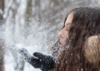 A young woman blows snow off her gloves. Falling snow