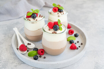 Dessert three chocolate in a glass jar with fresh blueberries, raspberries and blackberries on top on a gray concrete background. Dessert with three layers of different taste. Copy space.
