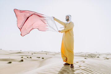 Handsome man from the emirates making a safari in the Dubai desert. Young man wearing the traditional kandura dress walking on the dunes