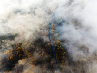 Aerial view of the highway among the autumn forest covered with fog