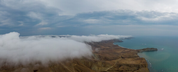A panorama of autumn hills covered with dense fog descending to the blue sea. Delightful landscape
