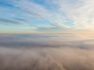 Aerial view of dense fog lying on the ground under the blue sky and the rays of the sunset