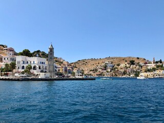 Symi clock tower. Symi island town centre and Aegean sea view. One of small Greek Dodecanese islands. Small marina with boats and yachts. Aegean Sea and island view. Turquoise blue water, colourful bu
