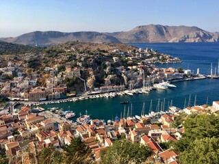 Fototapeta premium Symi island panoramic view from the top of hill. Greece. Aerial view. Marina, yachts, colourful houses, mountain. Dodecanese islands, Aegean sea. Greek island