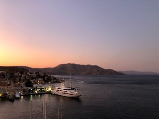 Fototapeta premium Sunset above Symi island, Greece. Dodecanese islands. Sunset above Symi island,Greece. Vanilla sky. Town lights, yacht moored in marina. Dream destination. Vanilla sky. Mountains
