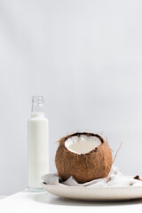 Una botella de leche de coco y un coco abierto sobre una mesa blanca	
