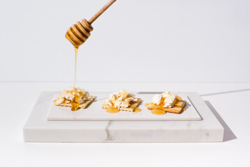 Verter la miel sobre tostadas de queso de cabra, con gotero de madera. Aperitivo comida mediterránea sobre fondo claro	