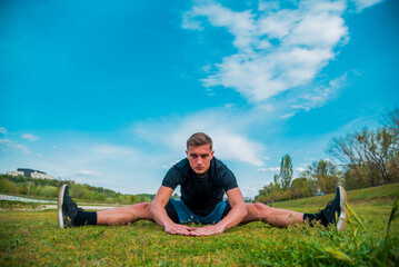 Naklejka na ściany i meble Flexible young man stretching legs outdoors