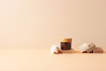 Jar of cosmetic cream with flowers and soap on pastel beige background. Close up, copy space