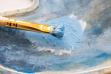 A brush with blue oil paint rests on the palette.