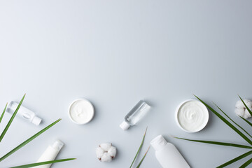 Cosmetic skin care products with flowers and palm leaf on grey background. Flat lay, copy space
