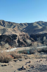 Panorama of the Charyn canyon with a clear blue mountain river running below, rocks on the front edge. Kazakhstan