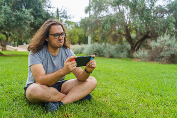 Angry man playing in the park with a handheld game console